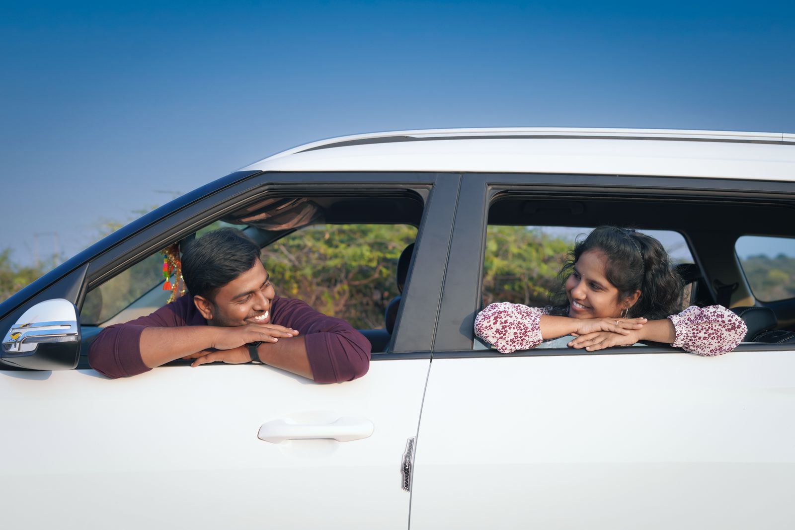 Happy couple smiling through the windows of their rental cars