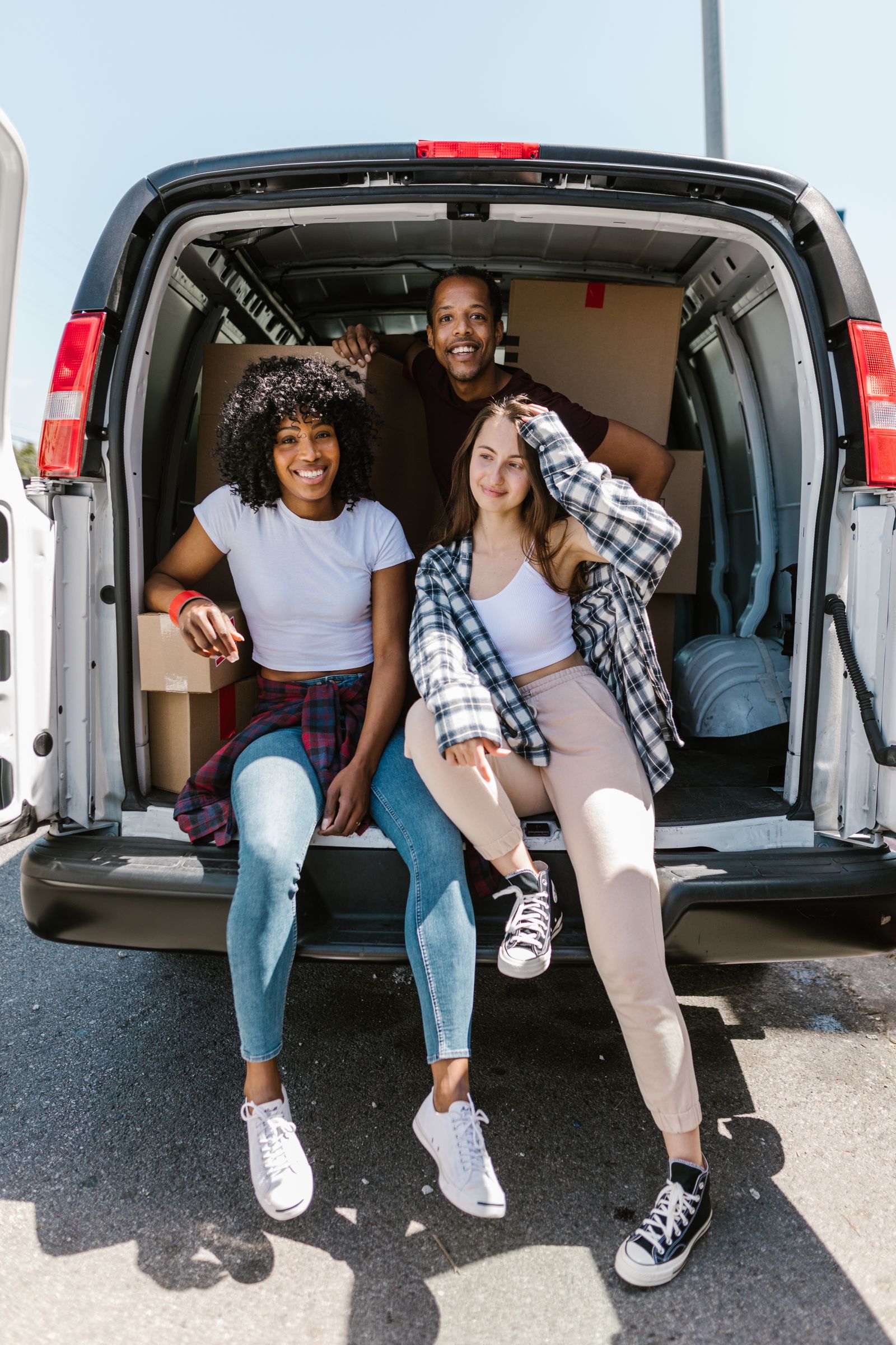 Three friends sit happily in a van, smiling and enjoying a sunny day outdoors.